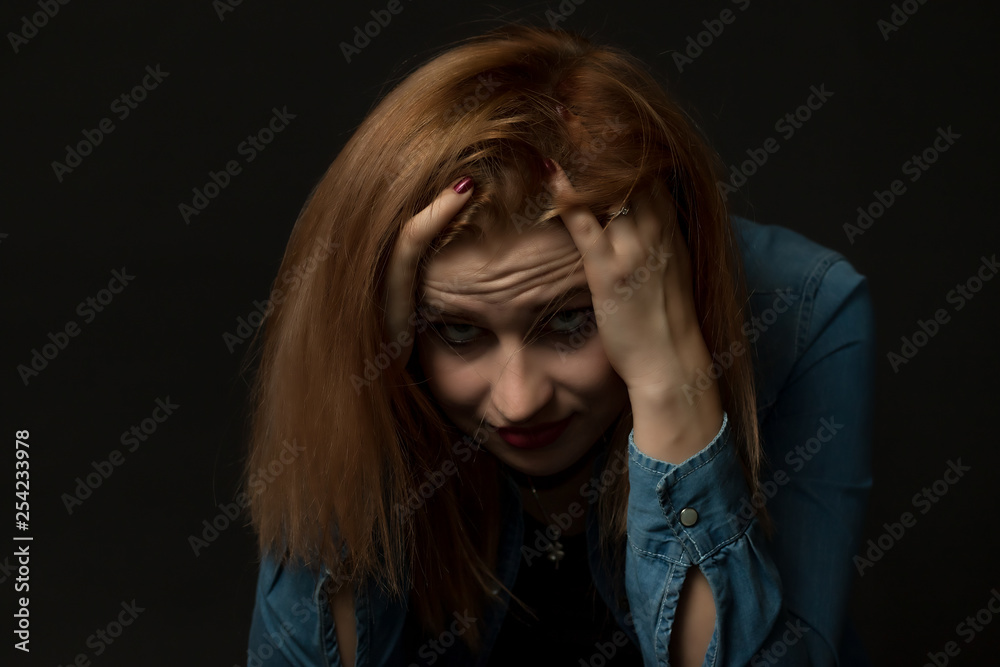 Low key portrait of young woman in trouble sitting and holding her head with both hands and looking at the camera. Low key portrait of young woman in trouble sitting and holding her head with both hands and looking at the camera.