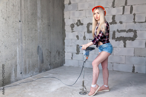 Closeup blonde girl foreman in white construction helmet holding professional mixer in house under construction. Concept worker, female labor, house under construction photo