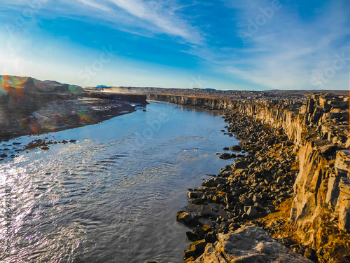 A river flowing in a stony gorge. The river has a calm flow. Some mist is splashing around the river bank. Blue sky with soft clouds. Sunny banks of the river. 