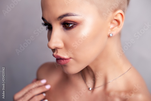 Closeup sexy blonde model with bright make-up, bare shoulders and short hair with shaved temples in modern round silver jewelry earrings and necklace. Сoncept shooting for bijouterie store