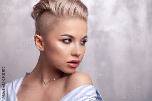 Closeup sexy blonde model with bright make-up, bare shoulders and short hair with shaved temples in modern round silver jewelry earrings and necklace. Сoncept shooting for bijouterie store
