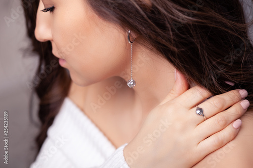 Closeup beautiful brunette girl with long hair in silver jewelry earrings, rings, bracelet, chain, necklace. Сoncept shooting jewelry store gentle, elegant, delicate, romantic bijouterie on model