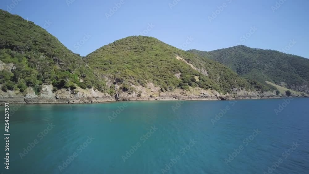 A slow moving aerial drone shot that travels around an island headland in a tropical paradise with crystal clear ocean waters below.