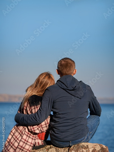 Tender couple is sitting near the picturesque lake and enjoying each other.
