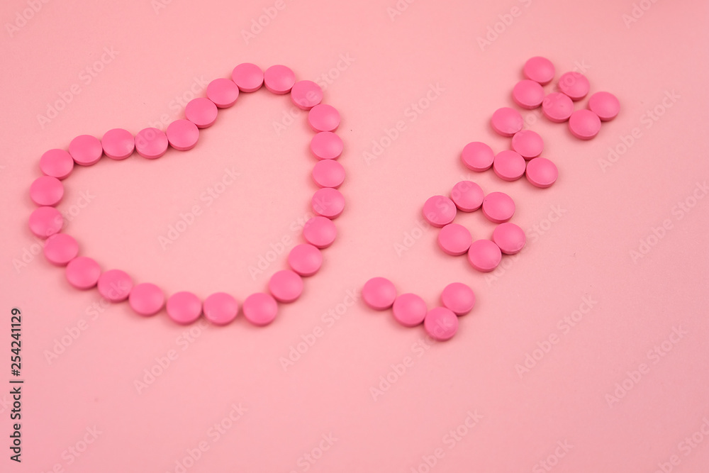 Close-up of heart shape word LOVE made of pink pills on pink background. Concept of Love is the best medicine.