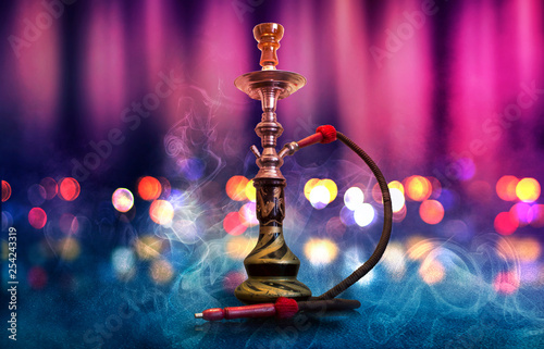 Hookah with smoke on the background of an empty scene, wet asphalt and colored neon light, blurry lights of the night city, bokeh