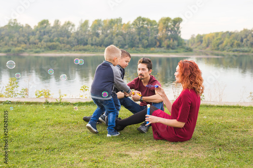 Family and nature concept - Mother, father and their children playing with colorful soap bubbles