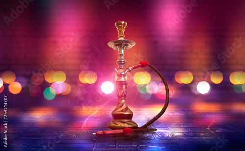 Hookah with smoke on the background of an empty brick wall, wet asphalt and colored neon light, blurry lights of the night city, bokeh