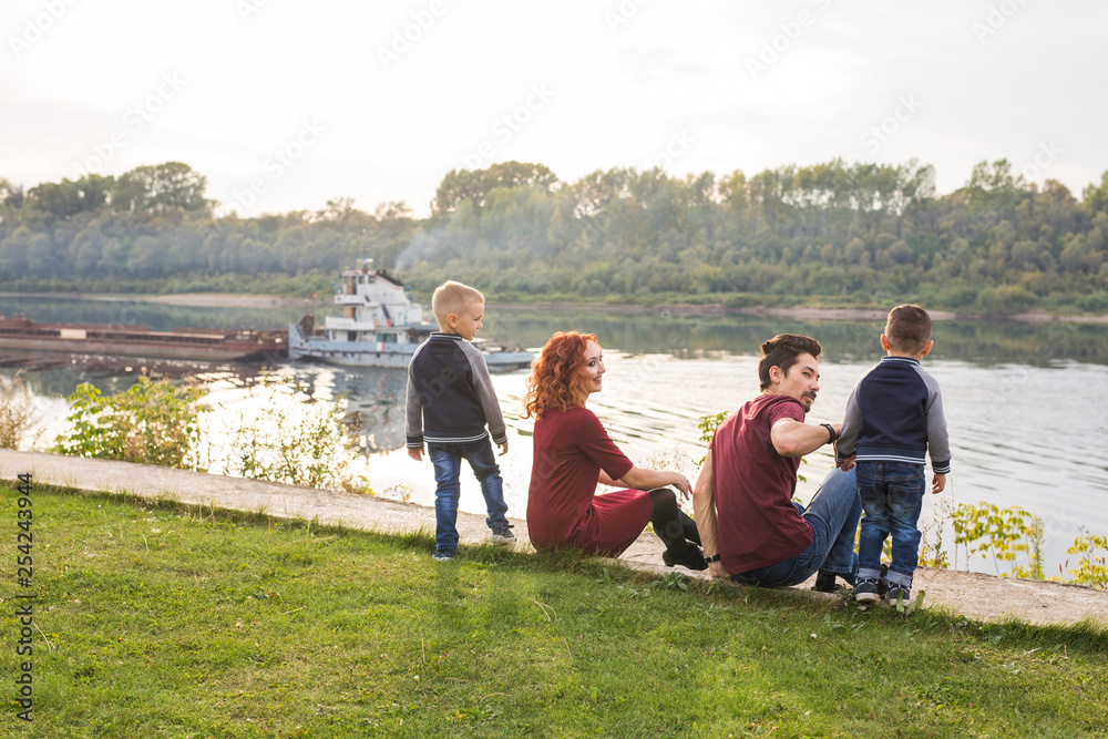 Parenthood, childhood and nature concept - Family sitting on the green ground and looking at small boat Parenthood, childhood and nature concept - Family sitting on the green ground and looking at small boat