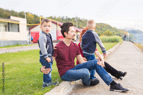 Parenthood, childhood and nature concept - Family sitting on the green ground and looking at small boat