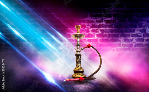 Hookah with smoke on the background of an empty brick wall, wet asphalt and colored neon light, blurry lights of the night city, bokeh