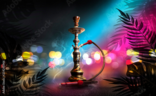 Hookah on the background of tropical leaves and a brick wall. Neon lights, laser shapes in the smoke, colorful bokeh
