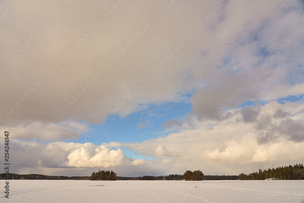 Two islands in the middle of Littoistenjärvi lake covered with ice and snow under a blue cloudy sky. Littoinen, Finland.