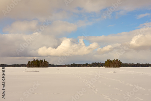 Two islands in the middle of Littoistenjärvi lake covered with ice and snow under a blue cloudy sky. Littoinen, Finland. photo