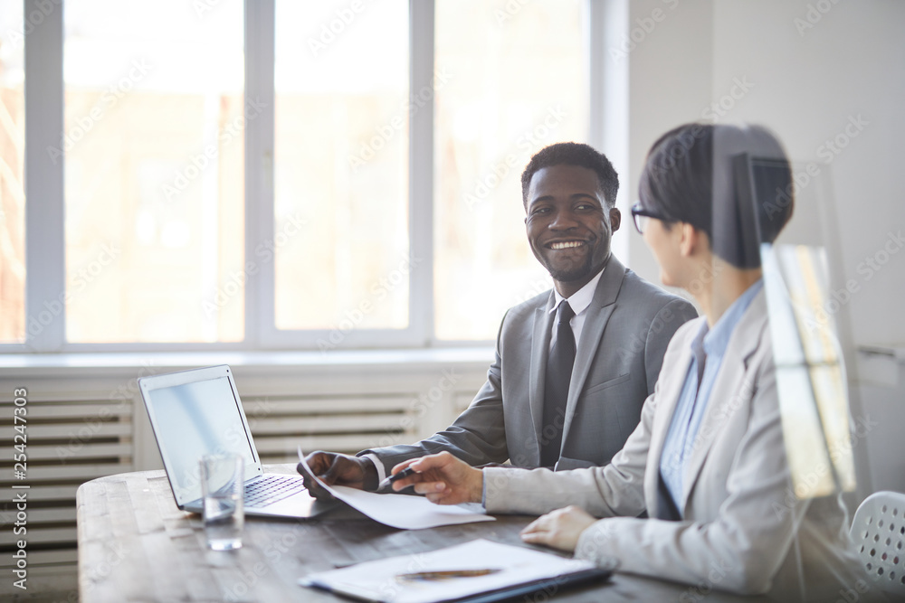 Young successful African-american businessman looking at his colleague while consulting about some points of paper Young successful African-american businessman looking at his colleague while consulting about some points of paper