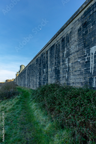 Valokuva A view a green grassy path along a huge fortress stone wall under a majestic blu