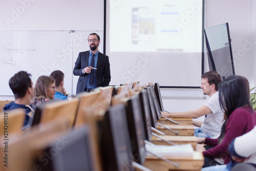 Group of students study with professor in modern school classroom. Male professor explain to students and interact with them, helping a students during class.
