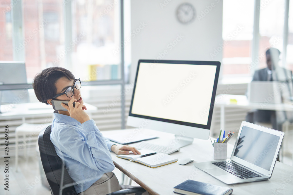Busy young employee or agent consulting client on the phone while sitting by desk in office