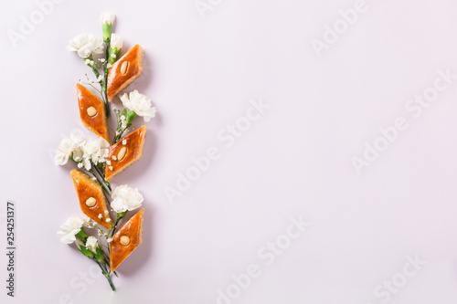 Novruz floral composition of traditional Azerbaijan pastry pakhlava or baklava with beautiful white flowers spring greeting card, lilac background, text translation: 