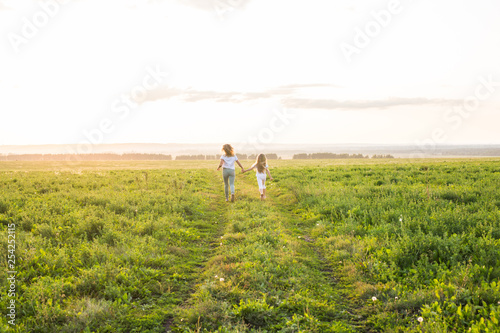 Family, summer and holiday concept - Mother holding her daughter's hand running in green field