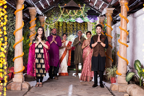 Family welcoming guests or in namaste / namaskara pose while looking at camera in celebration mood photo