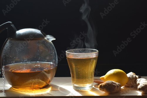 ginger tea in a tea pot and glass on a wooden board on a black background