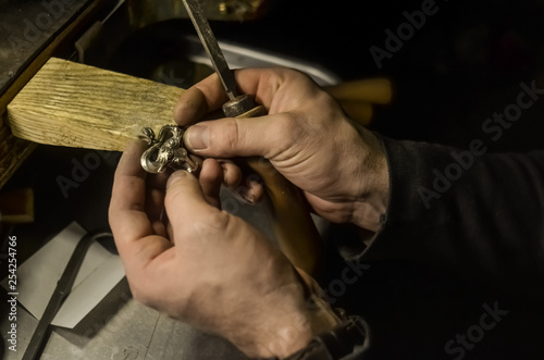 The master jeweler holds the working tool in his hands and makes jewelery at his workplace in the jewelry workshop. © Valerii