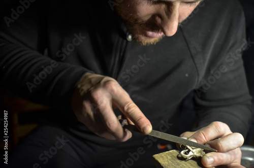 The master jeweler holds the working tool in his hands and makes jewelery at his workplace in the jewelry workshop.