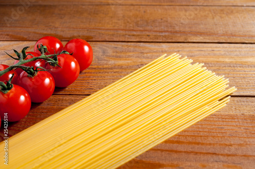 Spaghetti and cherry tomatoes on a wooden table. Spaghetti to the right of tomatoes. Homemade food or restaurant. Ingredients for cooking. National Italian healthy food.