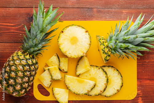 fresh ripe tropical pineapple cut into slices on a yellow rackside lying on a wooden table