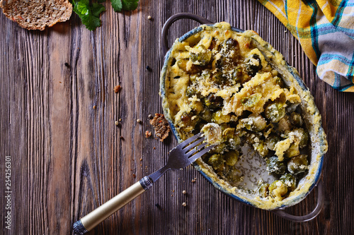 Delicious and healthy brussels sprouts baked in cream sauce with cheese and bread crumbs on a wooden table next to fork ready to eat, top view