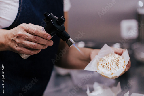 Tartlet with a meringue and kitchen torch blowtorch with blue flame. woman hand holdings blowtorch. bakery concept photo