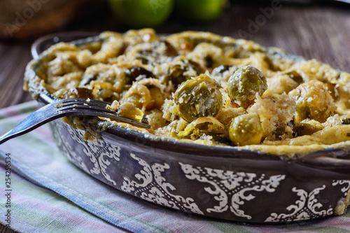 Delicious and healthy brussels sprouts baked in cream sauce with cheese and bread crumbs on a wooden table next to fork ready to eat