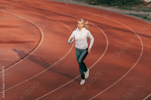 Caucasian female runner in sportswear running on the stadium with earphones in ears.