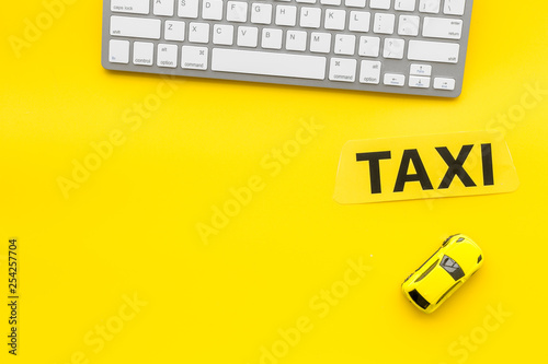 Taxi operator concept. Order taxi online. Sign ner car toy and keyboard on yellow background top view copy space