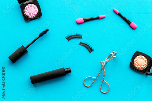 decorative cosmetic set with lash curler and mascara on blue woman desk background top view