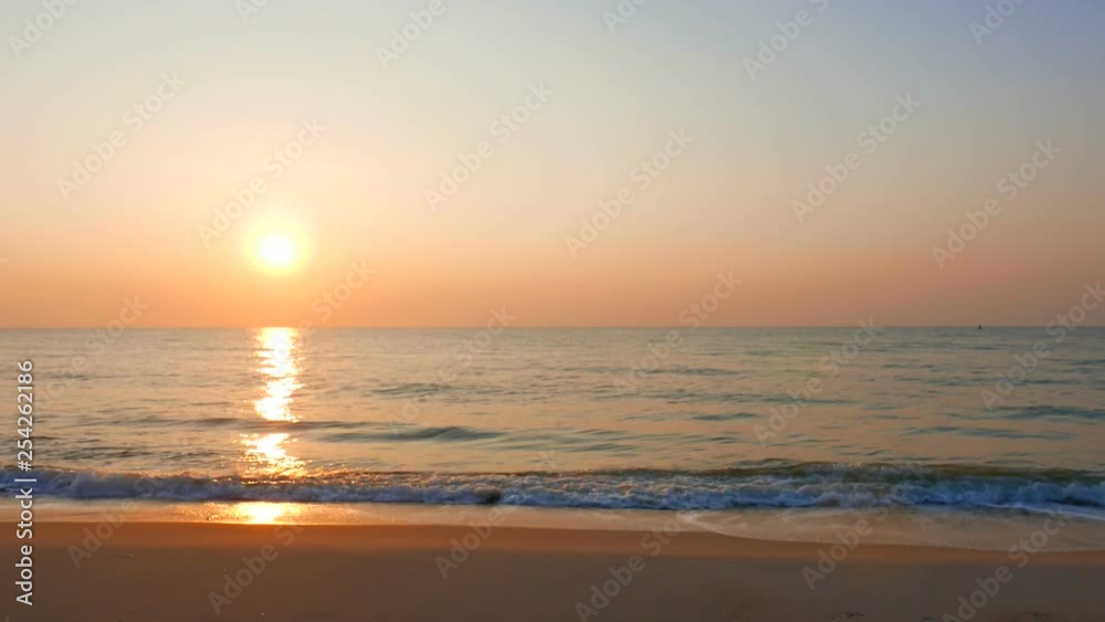 A landscape view of a sunset on the clear orange sky, the sun is reaching the horizon while waves are gently coming to the shore. A landscape view of a sunset on the clear orange sky, the sun is reaching the horizon while waves are gently coming to the shore.