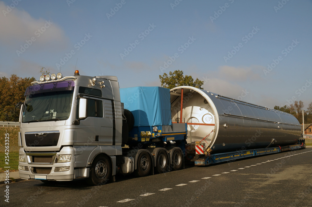 A view of a truck, a low-loader semi-trailer and an oversized cargo in the parking lot.