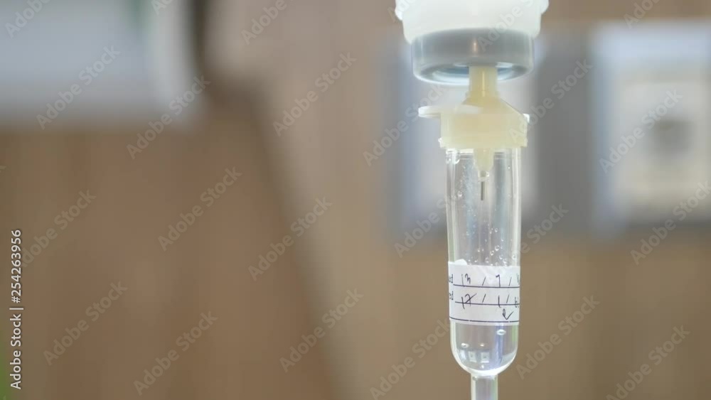 Saline drop in a drip chamber being infused along with medicine, and nutrients into a circulatory system of a patient, with a defocus of hospital patient room in the background Saline drop in a drip chamber being infused along with medicine, and nutrients into a circulatory system of a patient, with a defocus of hospital patient room in the background