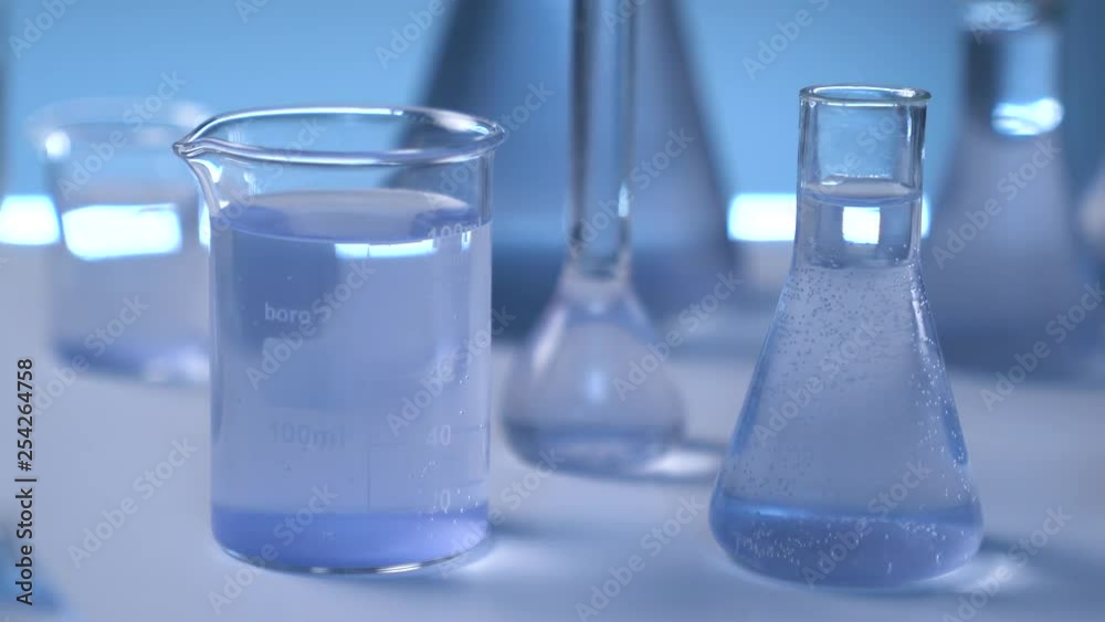On the table is a medical flask with liquid. The camera smoothly leaves the flask. Gray wall on background. Flasks in defocus on the gray background.