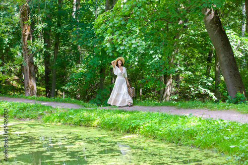 beautiful woman in a summer dress and hat walks along a forest path