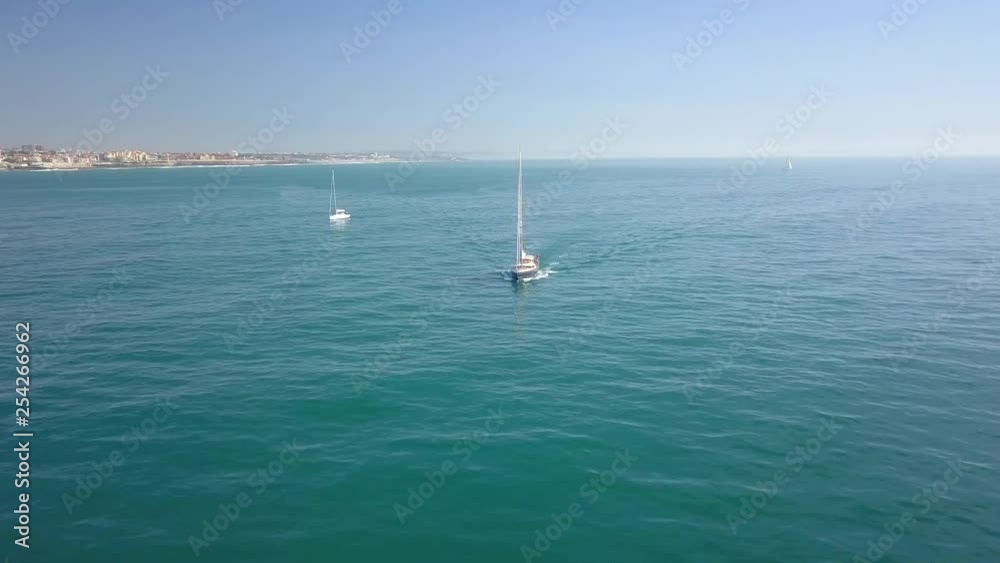 Aerial, drone shot, panning around a white sailboat, in the turquoise waters, of the Atlantic ocean, at the coast of Sao pedro do Estoril, on a sunny day, in Cascais, Portugal Aerial, drone shot, panning around a white sailboat, in the turquoise waters, of the Atlantic ocean, at the coast of Sao pedro do Estoril, on a sunny day, in Cascais, Portugal