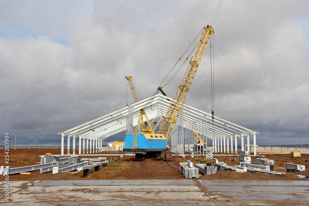 Large Crawler Crane against the background of blue sky while working. Construction of a metal frame of a new building.