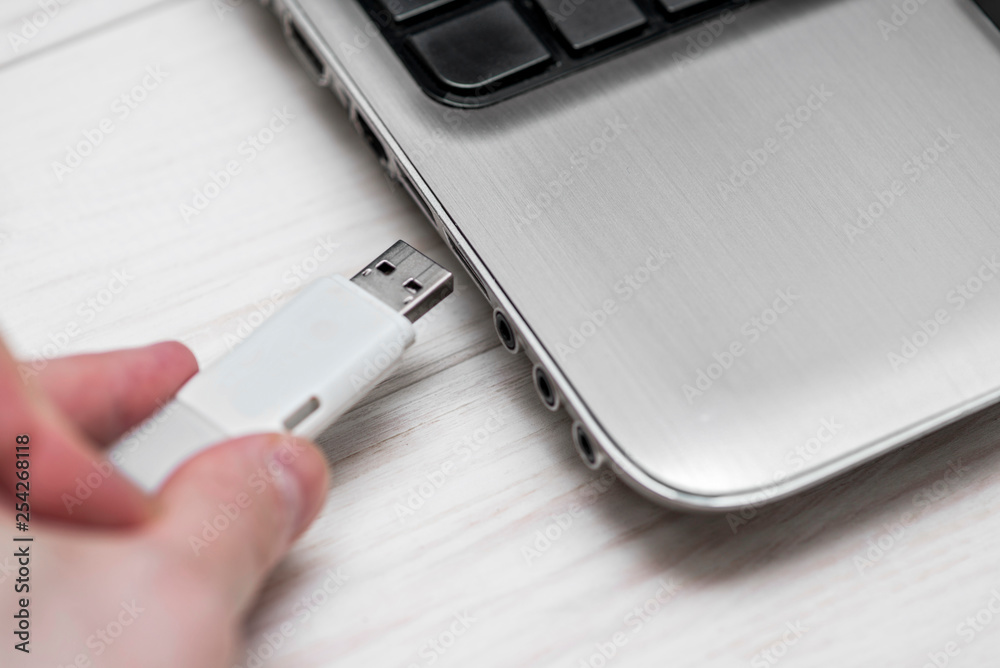 Plugging removable flash disk memory into laptop USB slot. Man hand inserting USB flash drive into laptop computer on wooden white background. Copying data from flash drive to laptop computer Plugging removable flash disk memory into laptop USB slot. Man hand inserting USB flash drive into laptop computer on wooden white background. Copying data from flash drive to laptop computer
