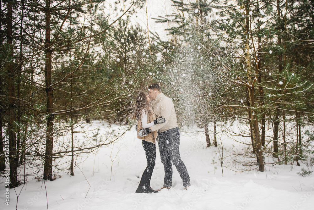 Winter love story on ice. Stylish lovers guy and girl in the winter forest throw snow and kiss