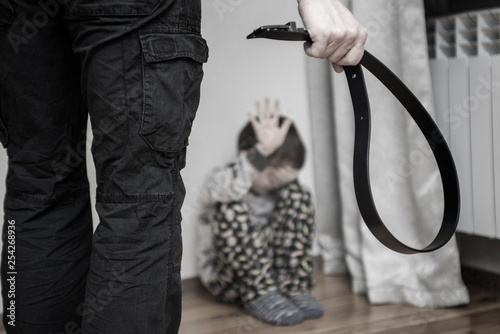 Obraz na plátně Aggressive parent with belt and frightened child in corner