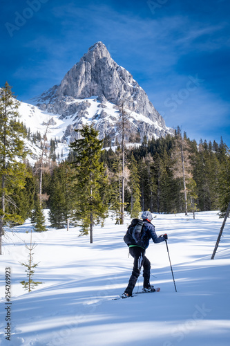 Man snowshoeing thruogh forest in Kaiserau with mountain Admonter Kalbling photo