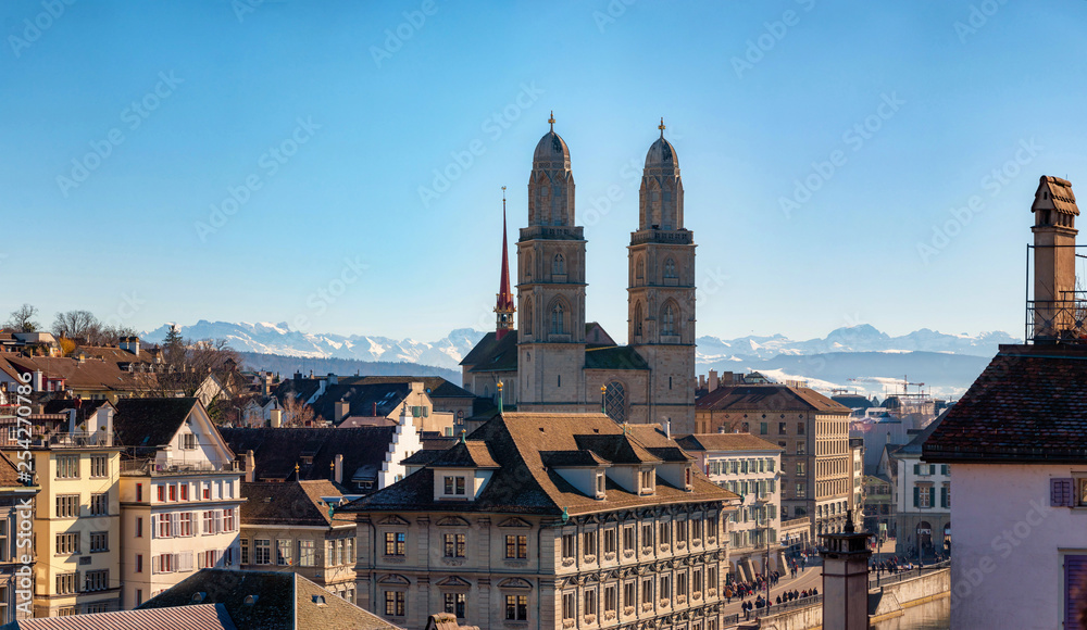 View on romanesque-style Grossmunster (Great Minster) and Zurich city center with Alps in the background, Zurich, Switzerland