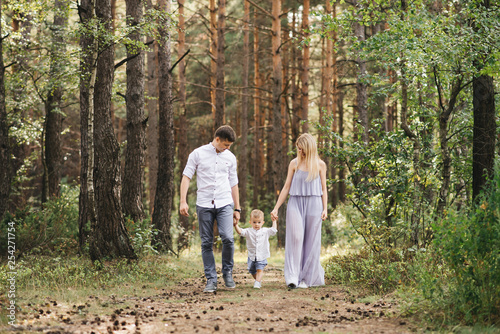 Happy young family spends time together in nature. Parents go and hold the child's hands