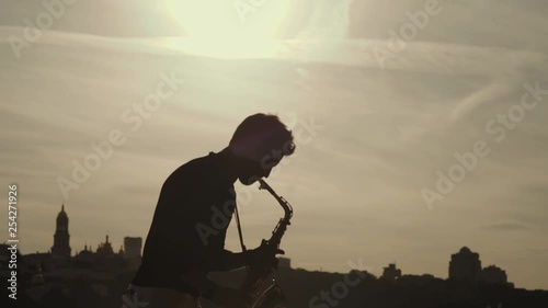 Saxophone player or saxophonist performing sax against sunset